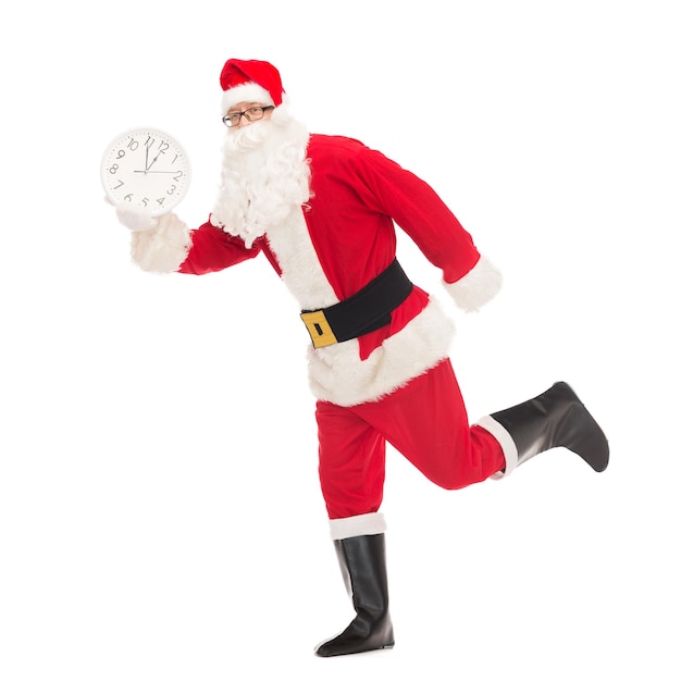 christmas, holidays and people concept - man in costume of santa claus running with clock showing twelve