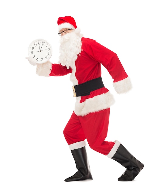 christmas, holidays and people concept - man in costume of santa claus running with clock showing twelve