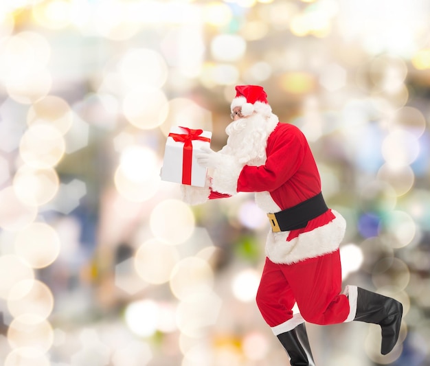 クリスマス、休日、人々のコンセプト-ライトの背景の上にギフトボックスで実行されているサンタクロースの衣装を着た男