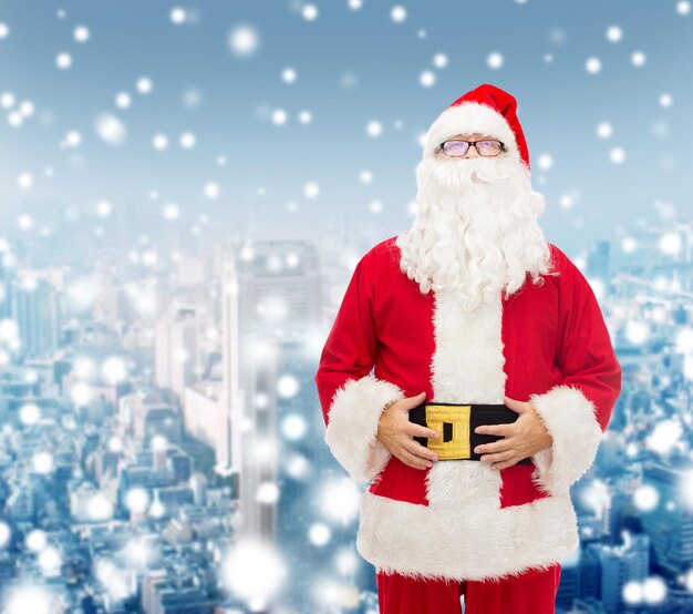 christmas, holidays and people concept - man in costume of santa claus over snowy city background