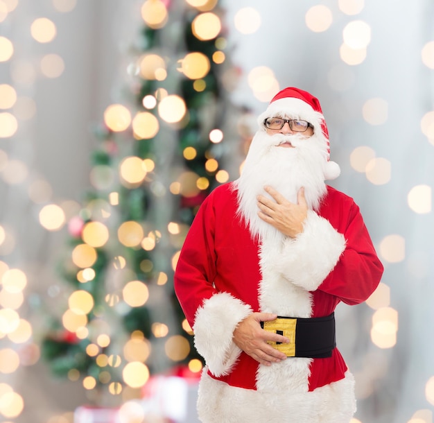 christmas, holidays and people concept - man in costume of santa claus over tree lights background