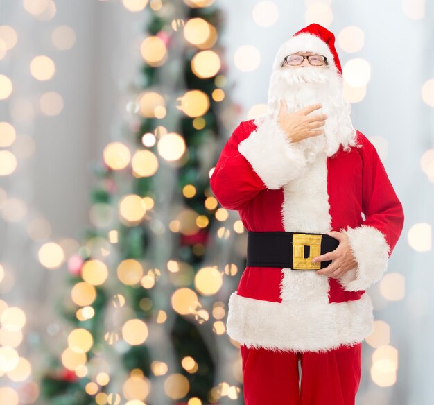 christmas, holidays and people concept - man in costume of santa claus over tree lights background