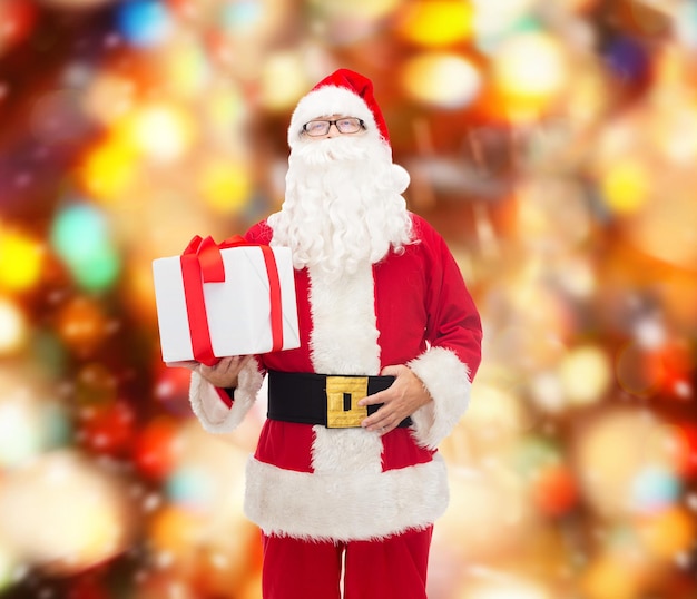 크리스마스, 휴일 및 사람 개념 - 빨간 불빛 배경 위에 선물 상자가 있는 산타클로스 의상을 입은 남자