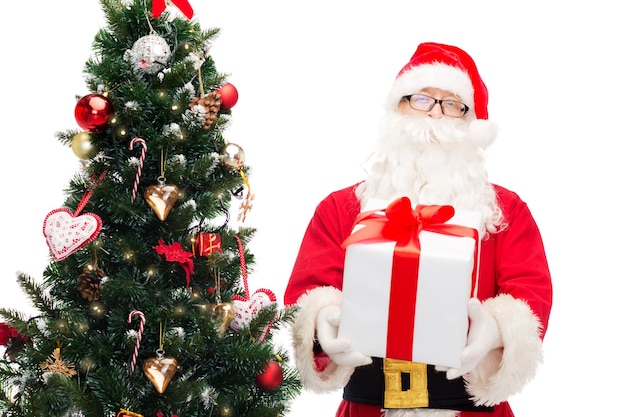 christmas, holidays and people concept - man in costume of santa claus with gift box and tree