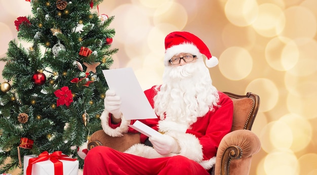 christmas, holidays and people concept - man in costume of santa claus with letter over beige lights background