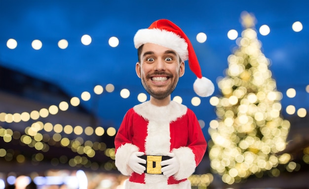 Christmas holidays and people concept smiling man in santa claus costume over lights background funny cartoon style character with big head
