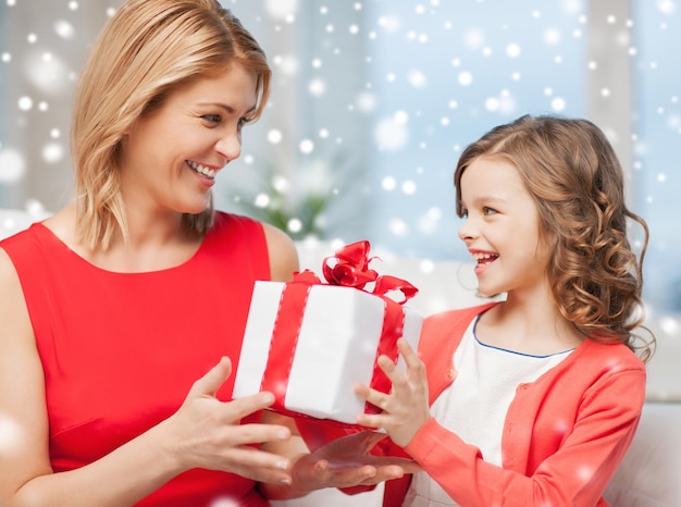 christmas, holidays, people and family concept - smiling girl receiving gift box from mother at home