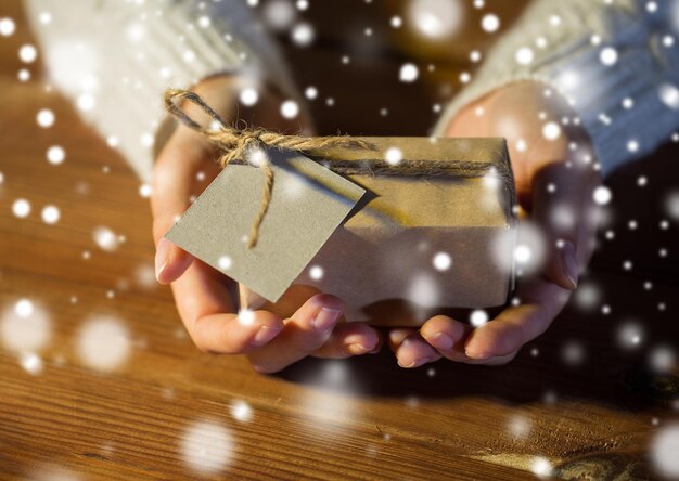 Photo christmas, holidays, presents, new year and people concept - close up of woman hands holding gift box or parcel wrapped into brown mail paper and decorated with fir brunch