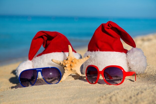 Christmas holidays and Romantic New Year at Sea. Santa hats and sunglasses on sandy beach