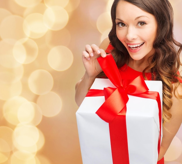 christmas, holidays, valentine's day, celebration and people concept - smiling woman in red dress with gift box over beige lights background