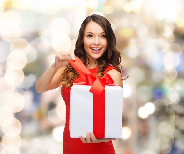 christmas, holidays, valentine's day, celebration and people concept - smiling woman in red dress with gift box over lights background