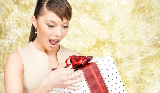 christmas, holidays, valentine's day, celebration and people concept - smiling woman in red dress with gift box over yellow lights background