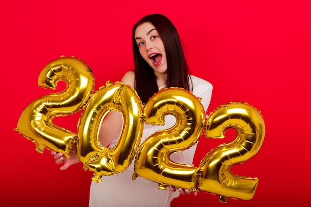 Christmas holidays - a young woman in a white dress holds the numbers 2022 on a red background