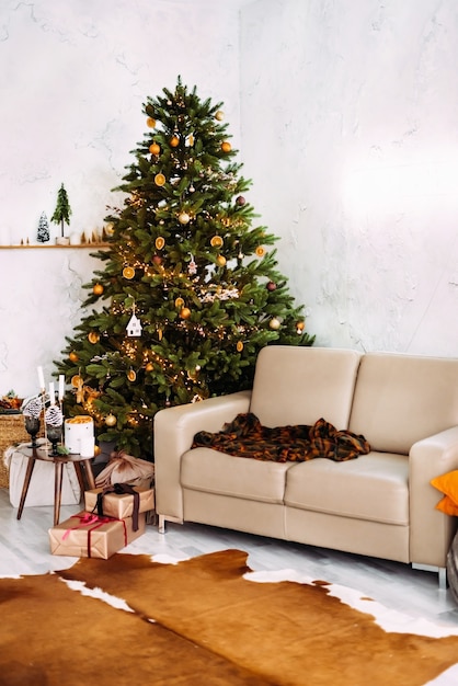 クリスマスツリーで飾られたソファ、ソファ、キャンドルと装飾が施されたテーブルを備えたクリスマスの家のインテリア。