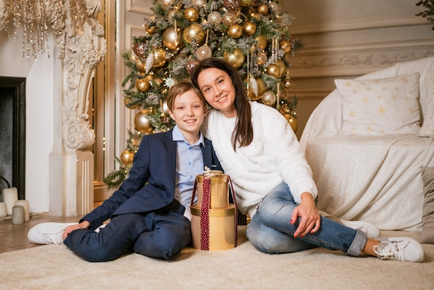 Christmas at home son and mom and dog under tree a boy and woman are playing with an animal celebrat...