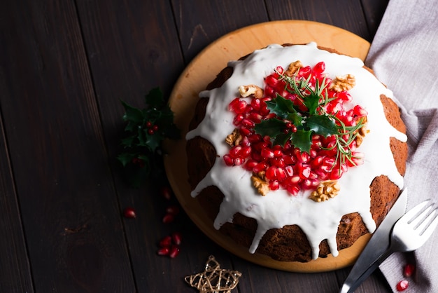 Christmas homebaked chocolate cake decorated with white icing and pomegranate kernels on a wooden dark , flat lay