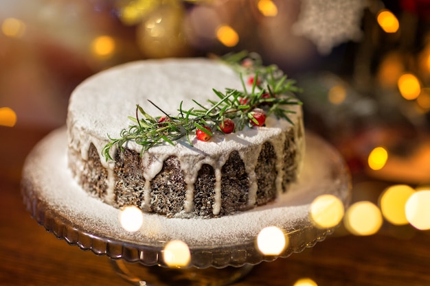 로즈마리와 크랜베리를 곁들인 크리스마스 홈메이드 케이크는 장식된 크리스마스 트리 옆에 서 있습니다