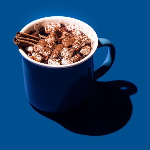 Рождество горячий шоколад в синей чашке на синем фоне в жестком свете.