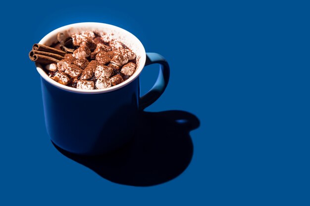 Christmas hot chocolate in a blue cup on a blue background.