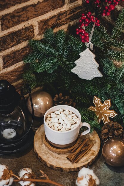 Cioccolata calda di natale con mini marshmellows in una vecchia tazza di ceramica con candele su un legno.