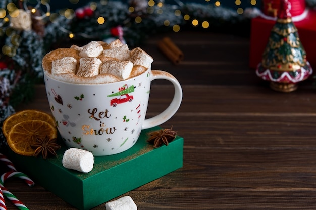 Christmas hot drink with marshmallows and spices on a background of snowy fir branches