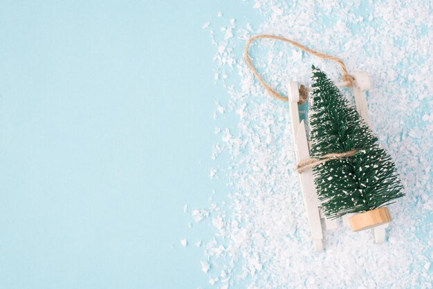 Il natale sta arrivando concetto. vista dall'alto dall'alto foto ravvicinata di un albero di natale in miniatura su una piccola slitta di legno bianca isolata su sfondo blu con copyspace