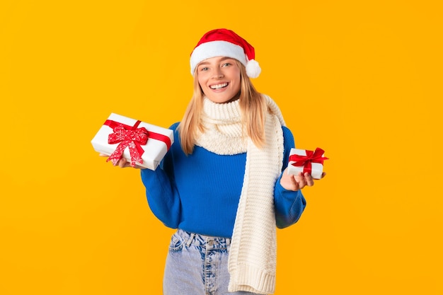 Christmas joyful woman in santa hat holding wrapped xmas gift boxes and smiling to camera posing