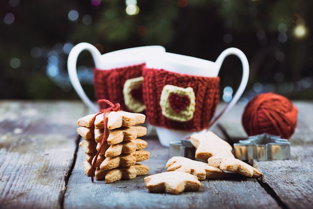 Foto natale - tazze di lana lavorate a maglia e pan di zenzero a forma di stella su un tavolo di legno