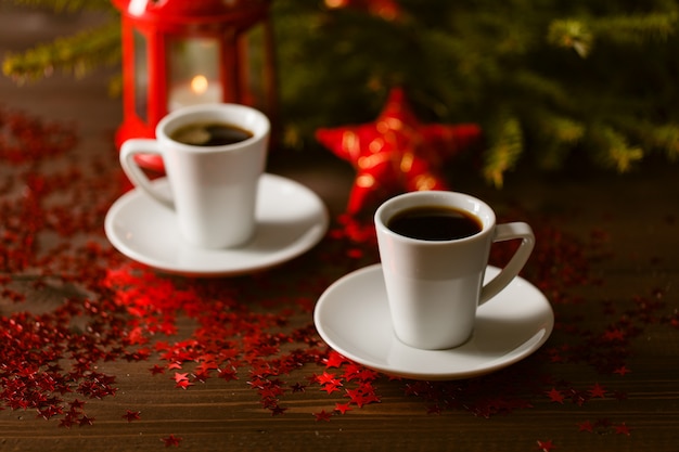 Christmas lantern glowing in dark with silver stars on red table with coffee