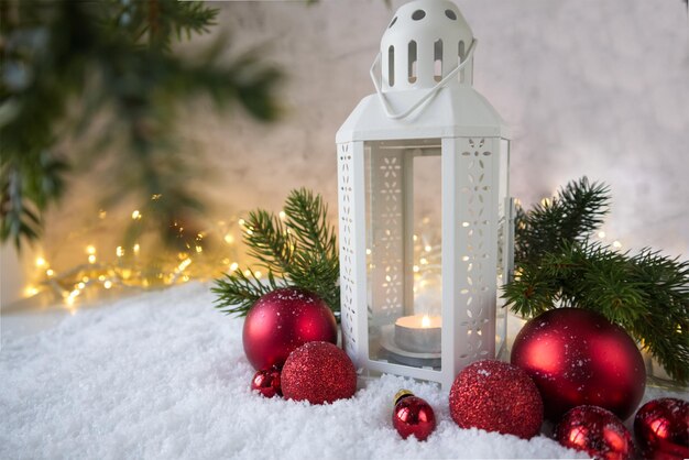 Christmas lantern on the snow next to red textured balls against the background of a lights