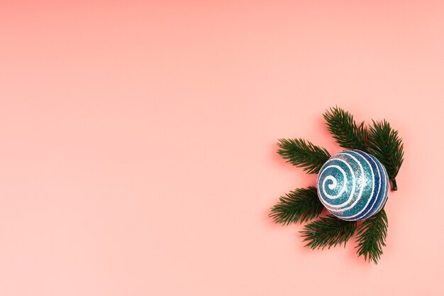 Christmas layout blue glitter Christmas ball with spruce branches on a pink background. Place for text, flat style, top view. Minimalistic Scandinavian style.