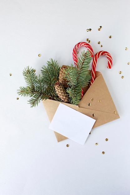 Christmas letter envelope with blank paper card, white gift box with golden ribbon bow, fir branches decorated balls on dark blue background. Flat lay, top view. Letter to Santa Claus concept.