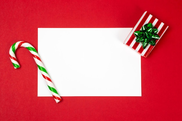 Christmas letter mock up blank white empty page on red\
background with a red and green candy cane and a gift box postcard\
greetings and thank you card template