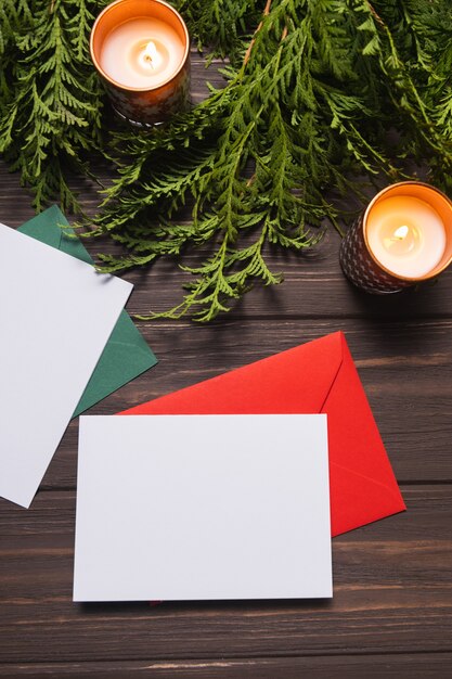 Christmas letters with greeting cards lie on a brown wooden table with fir branches and candles.