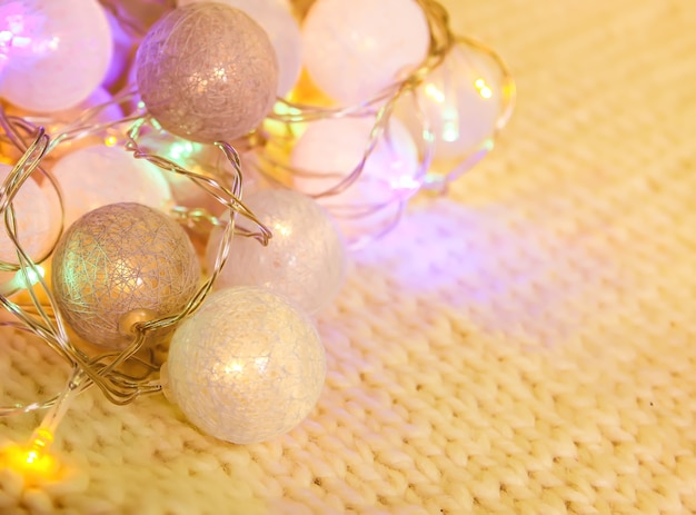 Christmas lights garland with round lanterns on knitted fabric background.