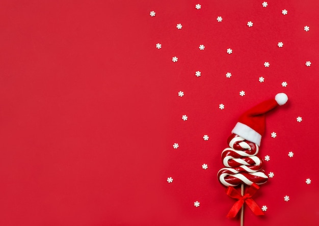 Christmas Lollipop in the shape of a Christmas tree with Santa red hat on red, top view