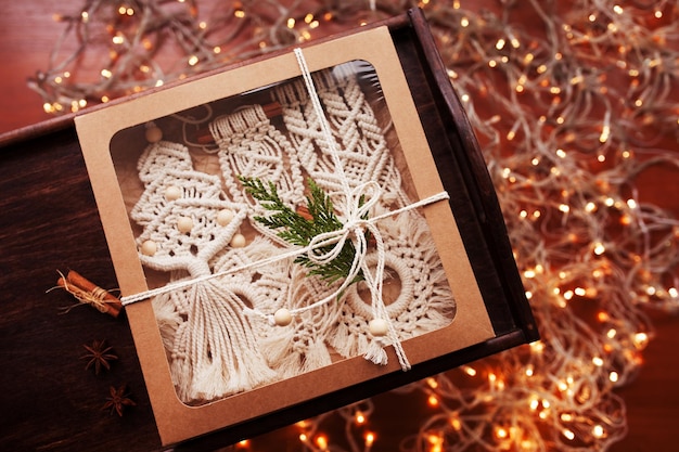 Christmas macrame box with toys on dark background natural\
materials cotton thread wood beads and stick eco decorations\
ornaments hand made decor winter and new year holidays