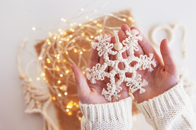 Decorazioni natalizie in macramè. fiocco di neve di natale su sfondo con luci sfocate. materiali naturali: filo di cotone. decorazioni ecologiche, ornamenti, decorazioni fatte a mano. vacanze invernali e di capodanno.