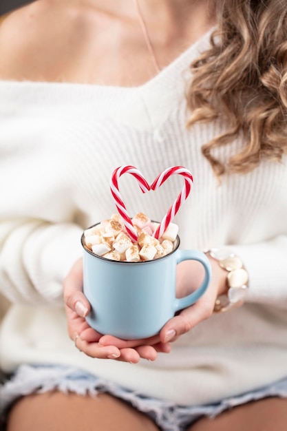 Christmas magic scene, cozy atmosphere. 
Woman holding cup of drink with marshmallows.