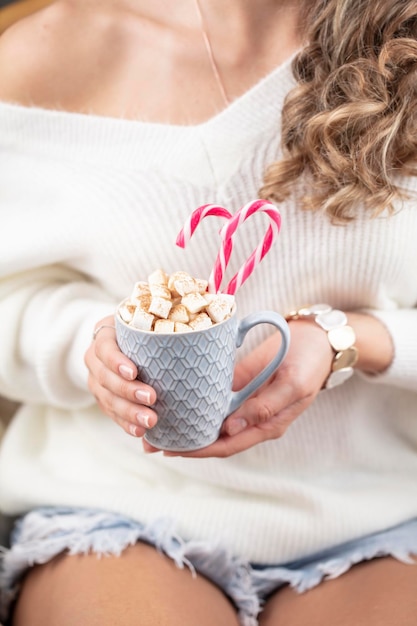 Christmas magic scene, cozy atmosphere. 
Woman holding cup of drink with marshmallows.