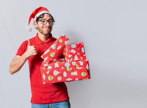 Christmas man holding gift boxes and smiling with thumb up\
smiling guy in christmas hat holding christmas gift boxes giving\
thumbs up friendly man in christmas clothes holding gift boxes