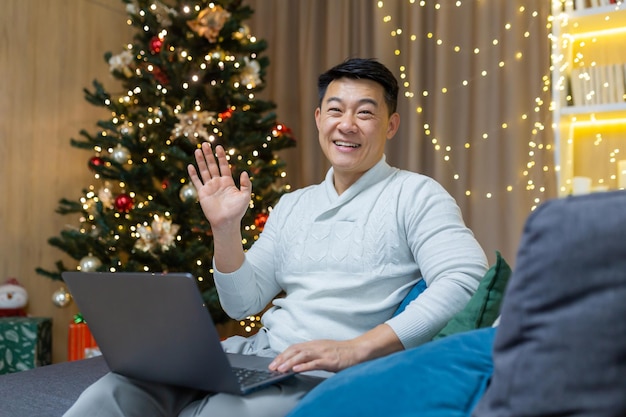 Christmas man at home on sofa smiling and looking at camera asian man near christmas tree with