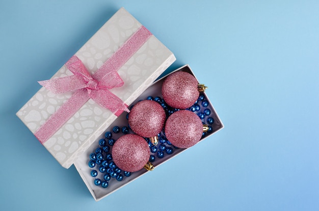 Christmas minimalistic composition. Opened gift box with baubles on pastel blue . Flat lay copyspace.  .