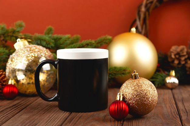 Christmas mock up of black mug on wooden table with festive decorations. Golden Christmas balls against red wall.