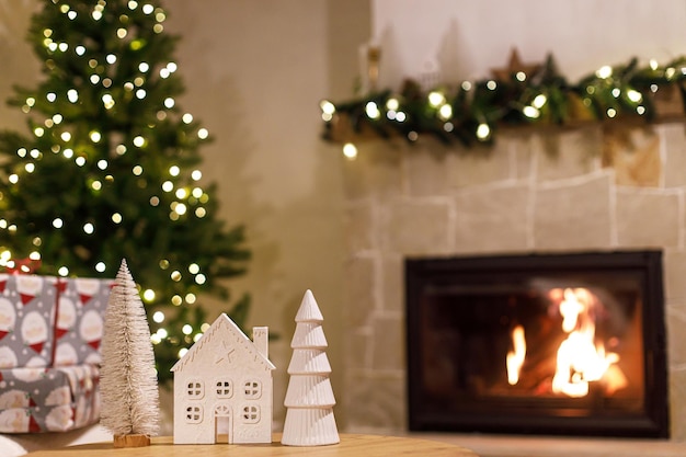 Decorazioni natalizie moderne sul tavolo contro il caminetto acceso atmosferico periodo natalizio elegante casa bianca e decorazioni ad albero nella sala festosa della vigilia di natale