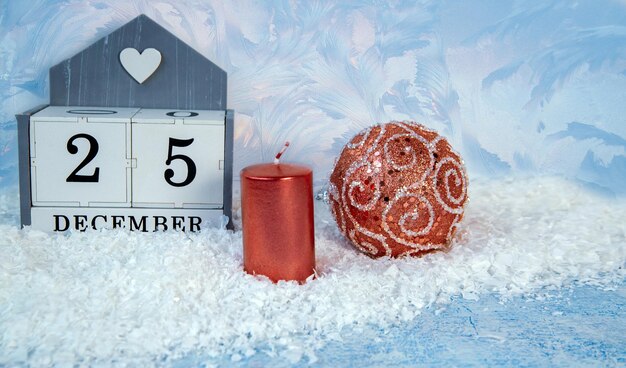 Christmas mood New Year background A sparkling Christmas ball on the snow a candle and a calendar with the date December 25 Holiday atmosphere