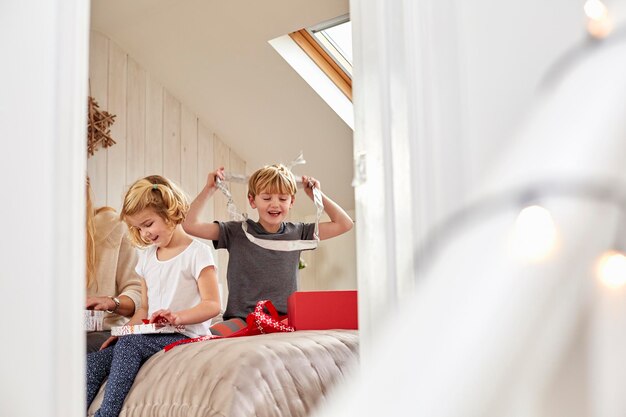 Christmas morning in a family home A mother and two children sitting on a bed opening presents