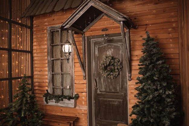 クリスマスの朝。クリスマスリースで飾られたドアのある小さな家をポーチします。冬のおとぎ話