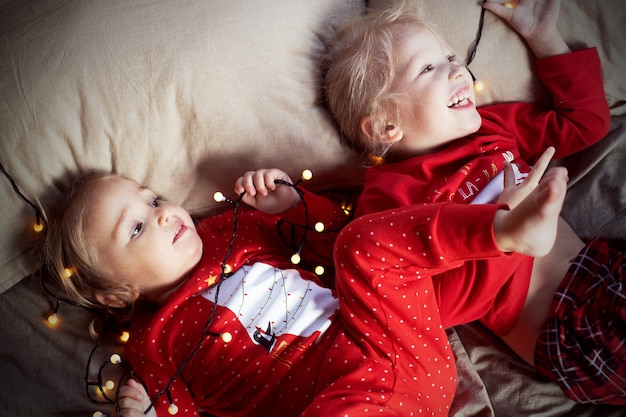 クリスマスの朝、楽しいベッドを持っている2人の子供の女の子の赤いパジャマ
