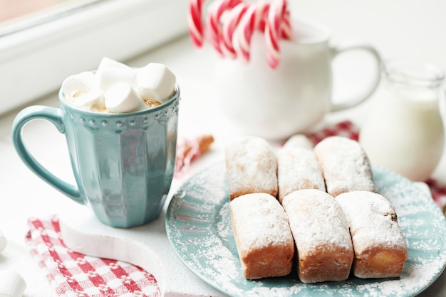 クリスマスのマフィン、ミルク、ココア、マシュマロ、窓辺の白い皿にキャンディロリポップ